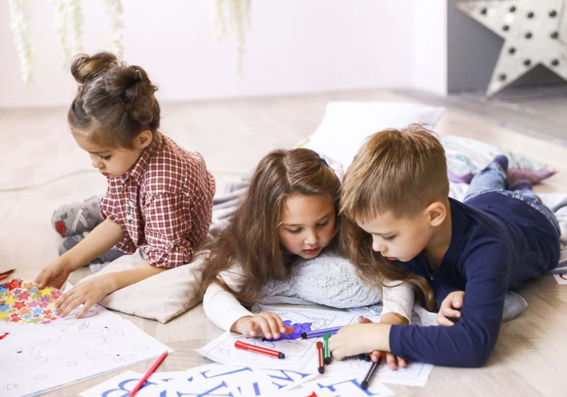 Three children sitting on a bed with colorful art supplies toptestbank